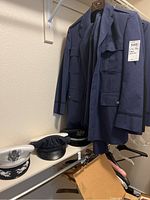 Jackets hanging on closet rack with white and black officers hats on shelf below, showing jackets in navy blue and black and hats with military insignia.