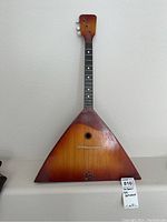Full view of the triangular wooden body and neck of the balalaika in sunburst finish.