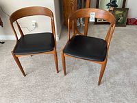 Front view of both chairs side by side on carpet, showing overall appearance, wood finish, and black vinyl seats