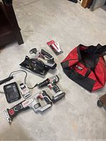 Photo of the set laid out on a concrete floor showing the reciprocating saw, circular saw, cordless drill, charger, two batteries, extra blades packet, and red and black Porter Cable tool bag.