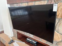 Front view of curved TV mounted above stone fireplace with stand pieces on floor