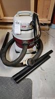Front view of Shop-Vac Allaround Wet/Dry Vacuum with hoses and two black plastic tube attachments next to it on the floor.