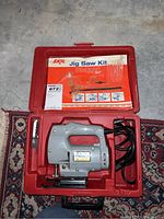 Full view of gray Skil jig saw Model 955 in red plastic carrying case with accessories stored in molded compartments inside the case.