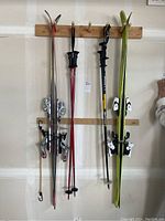 Full view of two pairs of skis and two sets of poles hung on wall hooks.