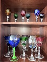 Display of colored wine glasses on bottom shelf, showing variety of colors and floral designs.