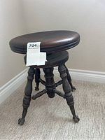 Side view of dark wooden adjustable stool with round seat and turned legs ending in claw feet casters.