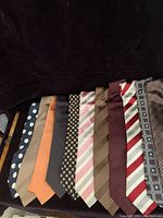 11 men's silk ties laid out side by side on a dark surface showing variety of patterns and colors.