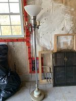 Full view of tall floor lamp showing overall height, milk glass shade, three candle lights around the pole, and cast base.