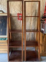 Two solid wood ladder shelf units side by side against a wall showing four shelves each and tapered wood frame.