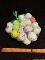 38 golf balls in a green mesh bag shown with a ruler for scale