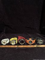 Full front view of all five watches in a row from left to right: white, yellow, red, orange, and black rubber bands with various dial styles.