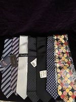 Seven new men's silk ties laid out flat showing a range of colors and patterns from diagonal stripes to polka dots and geometric patterns.