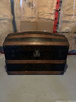 Front view of antique camel back steamer trunk showing dome top with wooden slats and dark body.