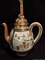 Front and side view showing handpainted figures and gold details on the teapot, with measuring stick indication about 8.75 inches tall.