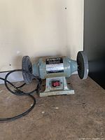 Frontal image of the Electric Delta bench grinder showing both grinding wheels, motor housing, red power switch, and base with some rust spots.