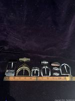 Full view of 5 belt buckles and 5 additional belt pieces laid next to a ruler for size reference