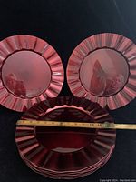 Stack of red ruffled edge dinner charger plates with a measuring tape showing about 13 inches in diameter.