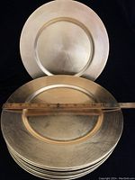 Stack of gold tone charger plates with a ruler showing approximately 12 inches diameter