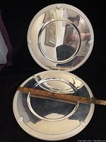 Four silver tone metal charger plates with shell edge design, showing two plates with rulers measuring approximately 13 inches diameter