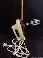 Photo showing the full body of the Iona Seabreeze electric hand mixer with attached power cord and metal beaters, positioned vertically.