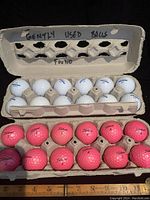 Photo of two open golf ball cartons with white Bridgestone and pink Titleist golf balls inside. The inner lid of one carton reads 'Gently Used Balls Found'.
