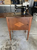 Full view of the vintage Singer sewing machine mounted in a wooden cabinet with four legs and foldable wooden extensions on the top surface.