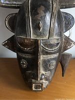 Close-up photo of mask's front face showing carved geometric details and facial features, some paint loss visible