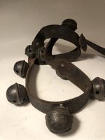 View of two leather straps each holding metal antique bells showing patina on surfaces and worn leather with fasteners.