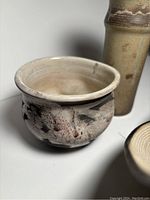 Close-up of the round pottery bowl showing mottled cream, gray, and red glaze with smooth interior and stamped signature on base.