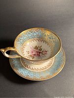 Front view of Aynsley teacup and saucer showing rose centre and gold turquoise ornate border