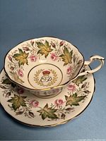 Full view of the teacup and saucer showing floral motif and royal emblem with initials E&D under crowned wreath
