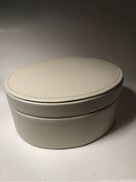 Closed oval cream leather trinket box showing smooth exterior and stitched lid