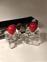 Two clear glass cube candleholders holding red globe candles with original black box behind them.