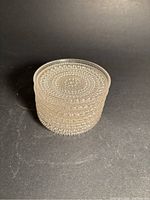 Stack of six clear glass coasters with raised bubble pattern viewed side on showing thickness and textured edge