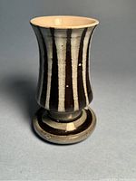 Front view of flared ceramic vase with black and cream vertical stripes on pedestal base.