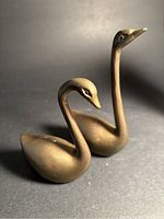 Front angled photo showing pair of brass swans, one with tall, straight neck and the other with curved neck.