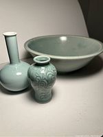 Wide view of all three ceramic and porcelain pieces showing the large bowl in back, narrow-neck vase left, and small round vase right with embossed design.