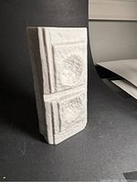 Front and side angled view of white bisque porcelain vase showing textured, raised square reliefs in Brutalist style.