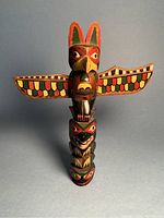 Front view of the wooden totem pole showing colorful painted faces and wings