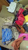 View of multiple purses on sofa including a blue patterned purse, leopard print purse with white handles, red handbag, tan and brown purses, and sets of gloves in brown and black leather-like material.