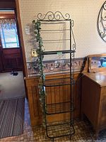 Front view of the narrow black metal baker's rack with four shelves, artificial vine on left side.