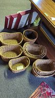 12 wicker baskets arranged on carpet near wooden table, showing their shapes and sizes clearly
