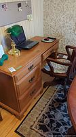 Wooden Roxton office desk with laptop, green desk lamp, and chair, showing side drawers and cabinet doors.