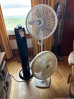 Photo showing all three fans together: two white Lasko oscillating fans (one tabletop and one adjustable height) and one black Utilitech tower fan standing side by side.