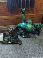 Photo showing a row of four ceramic animal figures on a wooden surface including a lion, dolphin, elephant, and part of a dog or bear.