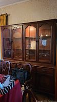 Front angle view of Gibbard buffet and hutch showing glass doors, shelving, and lower drawers with chairs in foreground.