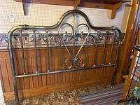 Full view of the king-sized metal headboard leaning against a wood-paneled wall showing the entire decorative design.