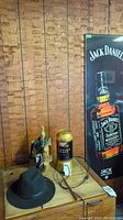 Jack Daniels poster board, Miller Draft lamp on wooden table, black Merino wool hat, Jack Daniels bandana on wooden decanter