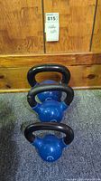 Photo showing all three kettlebells in a row from smallest to largest against a wood panel background.