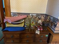 Wide photo of all items on wooden dresser including placemats, napkin rings, glasses, plates, wine carrier, and cast iron horse figure